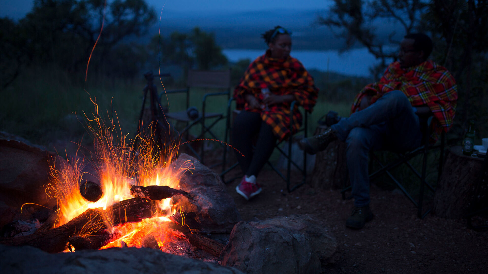 People sitting around a campfire with a view of Ihema Lake in the background