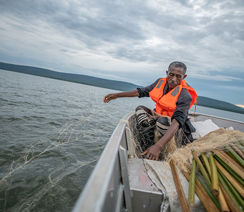 A man on a boat throwing a fish net into Lake Shakani.